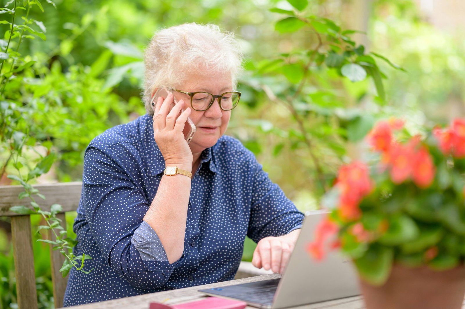 Senior woman taking on cell phone while using a laptop